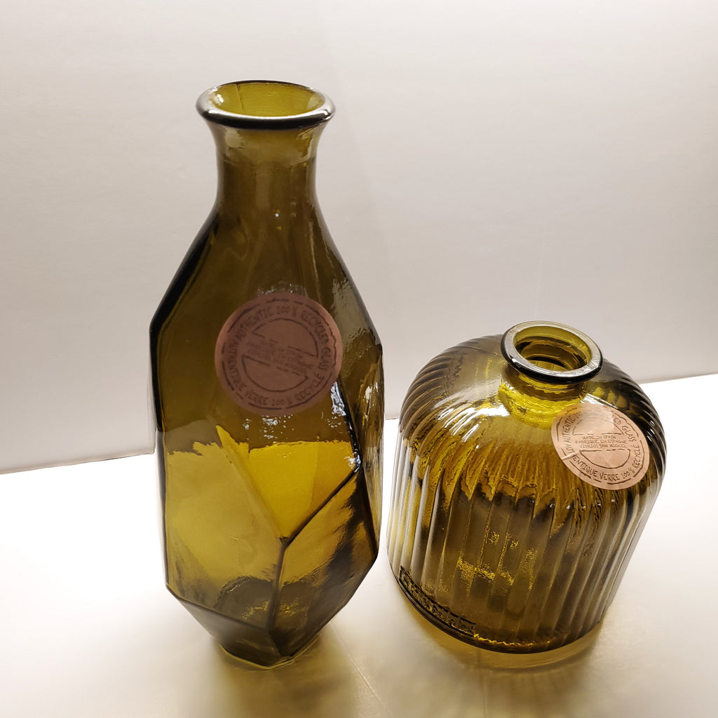 Two vintage amber glass bottles with round copper-colored labels, one standing upright and the other lying on its side, set against a plain off-white background.